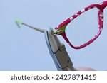 Small photo of Adjusting inclination on patchy red and white children eyeglass frame with conical nylon jaws inclination pliers.
