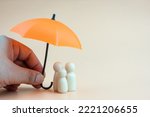 Insurance concept. Wooden family peg dolls with umbrella. Family, life, travel and health insurance. Orange background with copy space