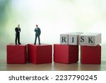 Risk assessment and risk tolerance concept : Miniature businessmen CEO, CFO talk negotiate on a company firm to manage risk. Two top leaders stand on wood cubes with word RISK