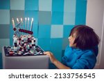 Small photo of boy in blue clothes looks at a cake pixels with a pickaxe and candles and lights in the studio. birthday five years
