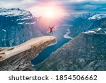 Norway, A woman Jump on the mountain's cliff edge of Trolltunga throning over Ringedalsvatnet  watching the sunset and snowy Norwegian mountains near Odda, Rogaland, Norway