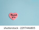 Thank you message on a pink heart sticky note on blue background 