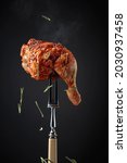 Small photo of Hot grilled chicken leg sprinkled with rosemary on a black background. Chicken drumstick on a fork.