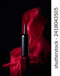 Small photo of Bottle of red wine and flutters of red cloth on a black background.