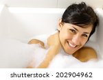 Cute young woman smiling in bath tub full of foam