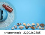 Summer and vacation flat lay with a beauty blue striped woman straw hat, sun glasses, Suntan oil and various seashells at the lower edge of the picture on blue background.