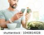 Small photo of Vitamins and energy. Pleasant satisfied unshaken man using cellphone holding and overlooking a broccoli.