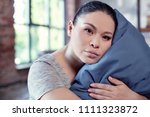 Small photo of Without sleep. Tired chivied woman hugging pillow and looking at camera