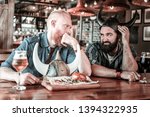 Small photo of Look of verjuice. Two bearded men sitting together in bar, with beer glasses in front of them, and frowning at each other.