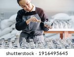 Small photo of Keen woman filing freshly cast vases, removing unnessesary bits, finishing them, making last touch. Behind a table with huge number of vases. In a pottery workshop.