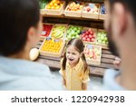 Small photo of Upset hysterical girl with closed eyes crying loudly while manipulating parents and standing against food stall in supermarket