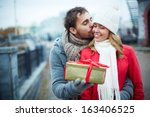 Image of affectionate guy kissing his girlfriend while giving her present outside