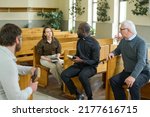 Small photo of Young African American priest with Bible talking to one of parishioners while explaining her some verses from New Testament