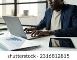 Hands of young African American businessman in formalwear sitting in front of laptop and typing while sitting by workplace in office