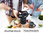 Close-up shot of hard-working food photographers looking through made photos on camera, served table for breakfast with fresh fruits, herbal tea, fried egg and lettuce