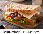 Small photo of A delicious ham and cheese sandwich with lettuce, tomato and dill pickle on a rustic wood table.