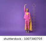 Little child is playing superhero. Kid is measuring the growth on the background of bright ultraviolet wall. Girl power concept. Yellow, pink and  purple colors.