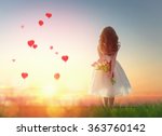 Sweet child girl looking at red balloons. Little child girl holding bouquet of flowers. Balloons in shape of heart flying in the sunset sky. Wedding, Valentine, love concept. 