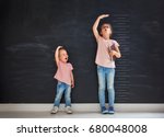 Two children sisters play together. Kid measures the growth on the background of blackboard. Concept of education.