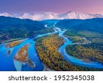 Small photo of Autumn view of the river bed with shallows of yellow trees after sunset against the background of high mountains, the Abakan river in Khakassia