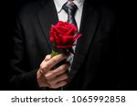 close up of man in black suit holding red rose.