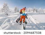 Snowboarder walking with a snowboard in the winter forest. Ski touring in the snowy mountains on a sunny day
