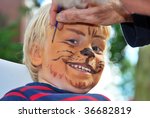 The face of a young child being made to look like a ferocious lion by a make-up artist
