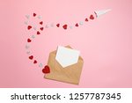 Distance love concept, sending love letter, valentines day. Kraft envelope with blank postcard and paper airplane flying on route made of heart shaped valentines cards lay on pink background desk