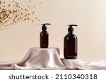Small photo of Dark amber glass pump bottle on satin cloth podium. Beige color background with dried flax flowers. Natural cosmetics products design.