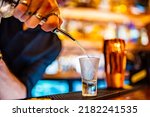 bartender pouring distilled alcohol into a shot glass in bar