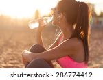 Beautiful fitness athlete woman drinking water after work out exercising on sunset evening summer in beach outdoor portrait