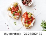 Small photo of Two bruschettas with ricotta cheese, olive and dried tomatoes on ciabatta bread on white background. Olive oil and spices decorated. Copyspace.