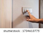 Small photo of Closeup of Asian woman finger is turning off on grey light switch over textile texture wall in the hotel. Copy space. energy saving.