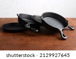 Small photo of pile of cast iron skillets on old wood table