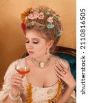 Small photo of Beautiful blonde woman dressed in Rococo period fashion as Marie Antoinette holding a glass of champagne.