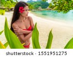 Beach beauty woman natural exotic girl in red swim wear bathing suit looking serene on tropical beach. Asian bikini model wearing hibicus flower for body care wellness and spa pampering.