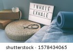 Small photo of Yoga breathing INHALE EXHALE sign at fitness class on lightbox inspirational message with exercise mat, mala beads, meditation pillow. Accessories for fit home lifestyle.