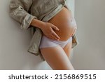 Pregnant woman wearing maternity underwear pajamas at home relaxing holding expecting tummy for skincare, health, lifestyle. Pregnancy belly closeup for cellulite and stretch marks