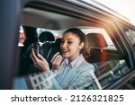 Good looking young business woman sitting on backseat in luxury car and fixing her makeup. Transportation in corporate business concept.