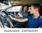 Driving instructor sitting his student and explain to him haw to properly hold steering wheel with both hands. Car driving school concept. View from inside.