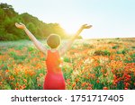Back view happy girl in red poppies flowers meadow in sunset light. A young woman in red dress arms raised up to the sky, celebrating freedom. Positive emotions feeling life, peace of mind concept.
