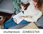 Top view relaxed young woman drawing work-life balance wheel sitting on the sofa with cat pet at home. Self-reflection and life planning. Coaching tools. Finding Balance in Your Life. Selective focus.