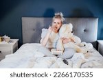 Heartbroken young woman huggying big teddy bear, eating ice cream from bucket while watching romantic movie on TV at home. Sad lady over breakup or relationship problems, feeling depressed and lonely.