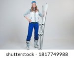 Smiling woman skier in a hat and mask for skiing. A young woman in clothes for skiing and outdoor activities. A woman holds skis and poses on a white background in the Studio.