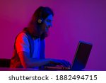 Online programming training, computer programmer or student. A young man with long hair and headphones. Use a laptop, neon tinting