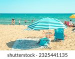 Small photo of Castelldefels, Barcelona, Spain - 07 31 2022: Beach scene with sunshades and people sunbathing and enjoying summer vacations.