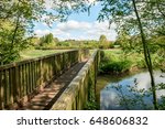 Bridge over reflective water - Perspective of wood bridge in English countryside crossing a river. The view is naturally framed with trees.