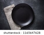 Black plate, cutlery and napkin on stone table top view. Table setting.