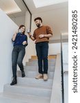 Small photo of A young man and woman enjoy a relaxing conversation on stairs while holding coffee mugs, embodying casual home life and companionship.