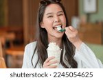 Small photo of happiness joyful asian young adult female woman teasing yummy smiling hand hold whipped cream in plastic cup,enjoy eating asia woman toothy smile while take a break with glass of dessert in cafe